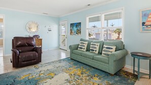 Un salon avec un canapé vert, un fauteuil en cuir marron et un tapis bleu et jaune.