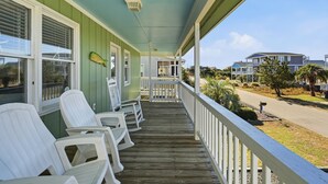 Une véranda en bois avec des chaises blanches, une façade verte et une vue sur les maisons voisines.