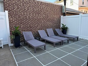 A patio with four lounge chairs and a white fence. - NEW 5BR Beach Retreat | Walk to Beach + Parking (Atlantic City)