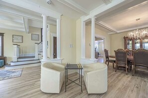 A spacious living room with a fireplace, a dining area with a chandelier, and a staircase leading to another level. - Grand Richmond Beach Retreat (Atlantic City)
