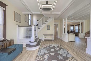 A spacious living room with a staircase, a blue sofa, a patterned rug, and a view into the dining area. - NEW 5BR Beach Retreat | Walk to Beach + Parking (Atlantic City)