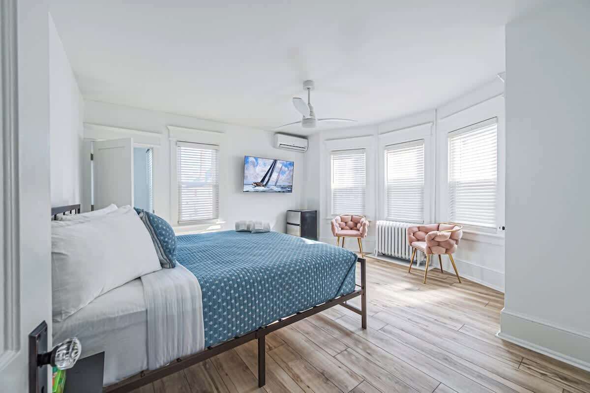 Een slaapkamer met een bed, een televisie, een plafondventilator en een raam met zonwering.