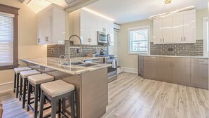 Una cocina moderna con una isla central, taburetes de bar y un ventanal grande.