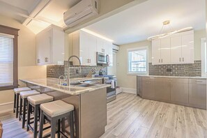 A modern kitchen with a central island, bar stools, and a large window. - Grand Richmond Beach Retreat (Atlantic City)