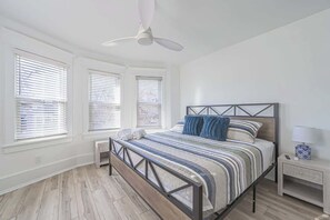 A bedroom with a bed, a nightstand, a ceiling fan, and windows with blinds. - Grand Richmond Beach Retreat (Atlantic City)