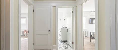 Un pasillo con una puerta blanca, piso estampado y vista a un área de cocina.