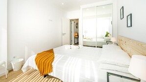 A modern hotel room with a large bed, a wooden headboard, a white nightstand, and a mirror. - Two bedroom apartments close to train station by Lisbon with Sintra (Sintra)