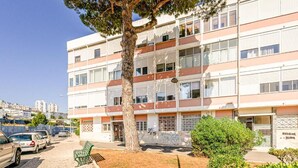 A multi-story building with a tree in front, a bench, and a small garden area. - Two bedroom apartments close to train station by Lisbon with Sintra (Sintra)