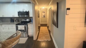 A modern kitchen with white cabinets, a microwave, and a stove. A hallway with a patterned rug leads to a door. - Serene 4-bedroom house perfect for relaxing stays in Decatur near Atl downtown (Decatur)