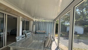 Un patio cubierto con una mesa y sillas, una banca acolchada y vista al jardín trasero.