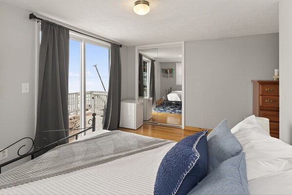 A bedroom with a large bed, a wooden dresser, and a view of a balcony. - Lakefront | Pet Friendly | Hot Tub | FLX Wineries (Seneca Falls)