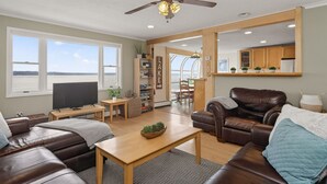 Una sala de estar con un sofá de cuero marrón, una mesa de centro de madera, un televisor y vistas al lago a través de amplios ventanales.