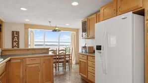 Una cocina con armarios de madera, un refrigerador blanco y un comedor con vistas al mar.