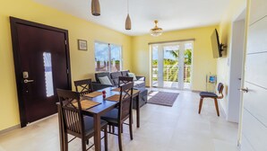 Spiseområde med bord, stole, sofa og et tv ophængt på væggen.