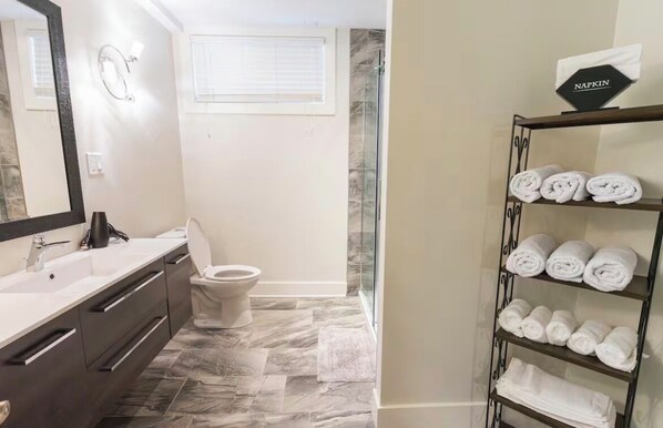 A bathroom with a white sink, dark-toned vanity, a toilet, and a towel rack with neatly folded towels.