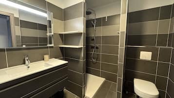 Une salle de bain moderne équipée d’un lavabo, d’un miroir, d’une douche et de toilettes.