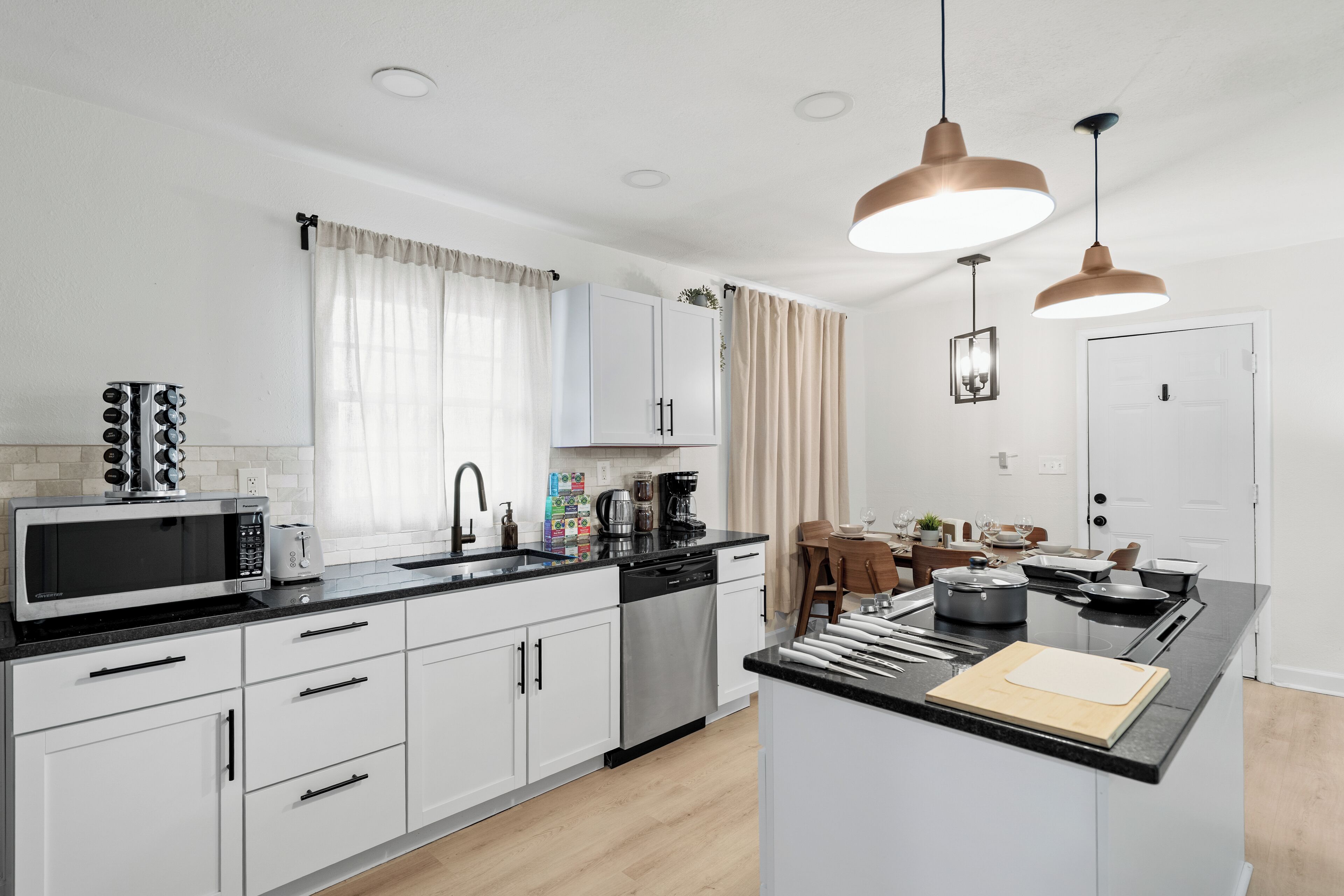 Una cocina moderna con armarios blancos, encimera negra, microondas, cafetera y lámparas colgantes.