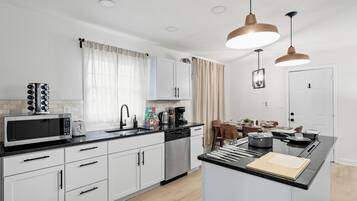 Una cocina moderna con armarios blancos, encimera negra, microondas, cafetera y lámparas colgantes.