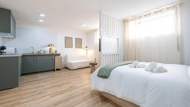 A modern hotel room with a wooden floor, a bed with white bedding, a small desk with a lamp, and a window with curtains. - Le Atelier by Lisbon with Sintra (Cascais)