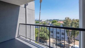A balcony with a view of a cityscape, including buildings and a palm tree. - Polished 1BR Hollywood Apt w Rooftop Pool & Views (Los Angeles)