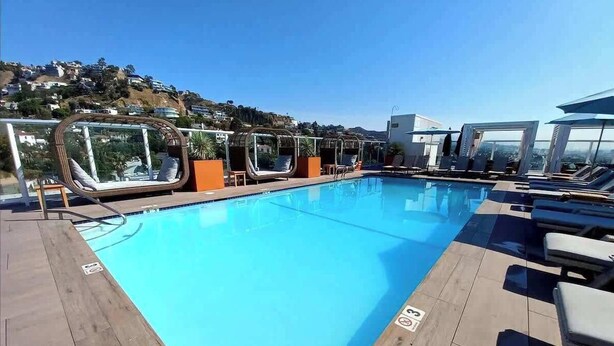 A rooftop pool with lounge chairs and cabanas, surrounded by a wooden deck and a view of a hillside. - Polished 1BR Hollywood Apt w Rooftop Pool & Views (Los Angeles)