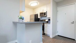 A compact kitchen with white cabinets, a microwave, and a refrigerator. - Polished 1BR Hollywood Apt w Rooftop Pool & Views (Los Angeles)