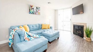 A modern living room with a blue sectional sofa, a fireplace, and a large window. - Polished 1BR Hollywood Apt w Rooftop Pool & Views (Los Angeles)