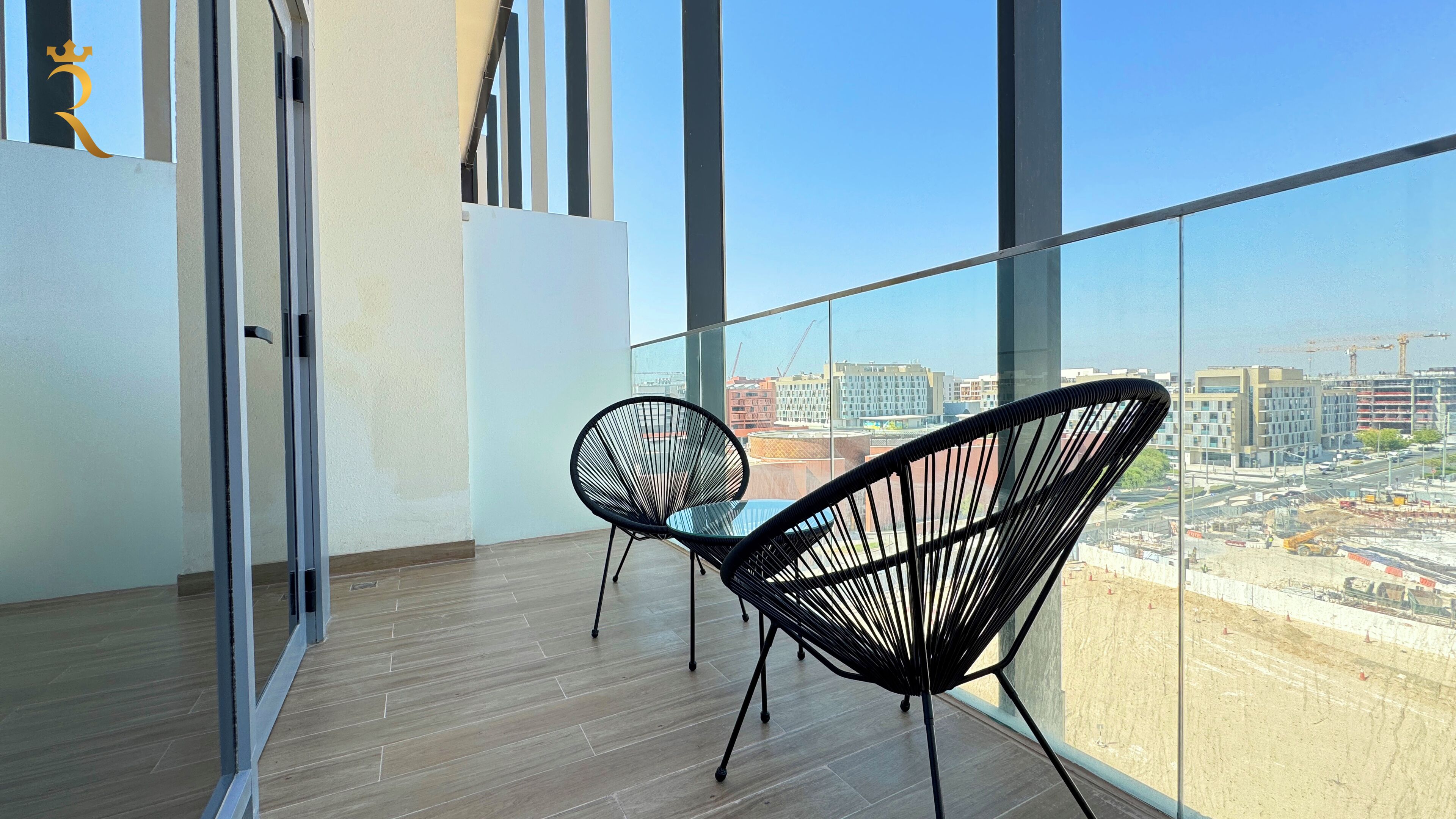 Un balcon avec deux chaises au design épuré en fil de fer noir, un plancher en bois et une vue sur la ville à travers de grandes fenêtres.