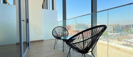 Un balcon avec deux chaises au design épuré en fil de fer noir, un plancher en bois et une vue sur la ville à travers de grandes fenêtres.