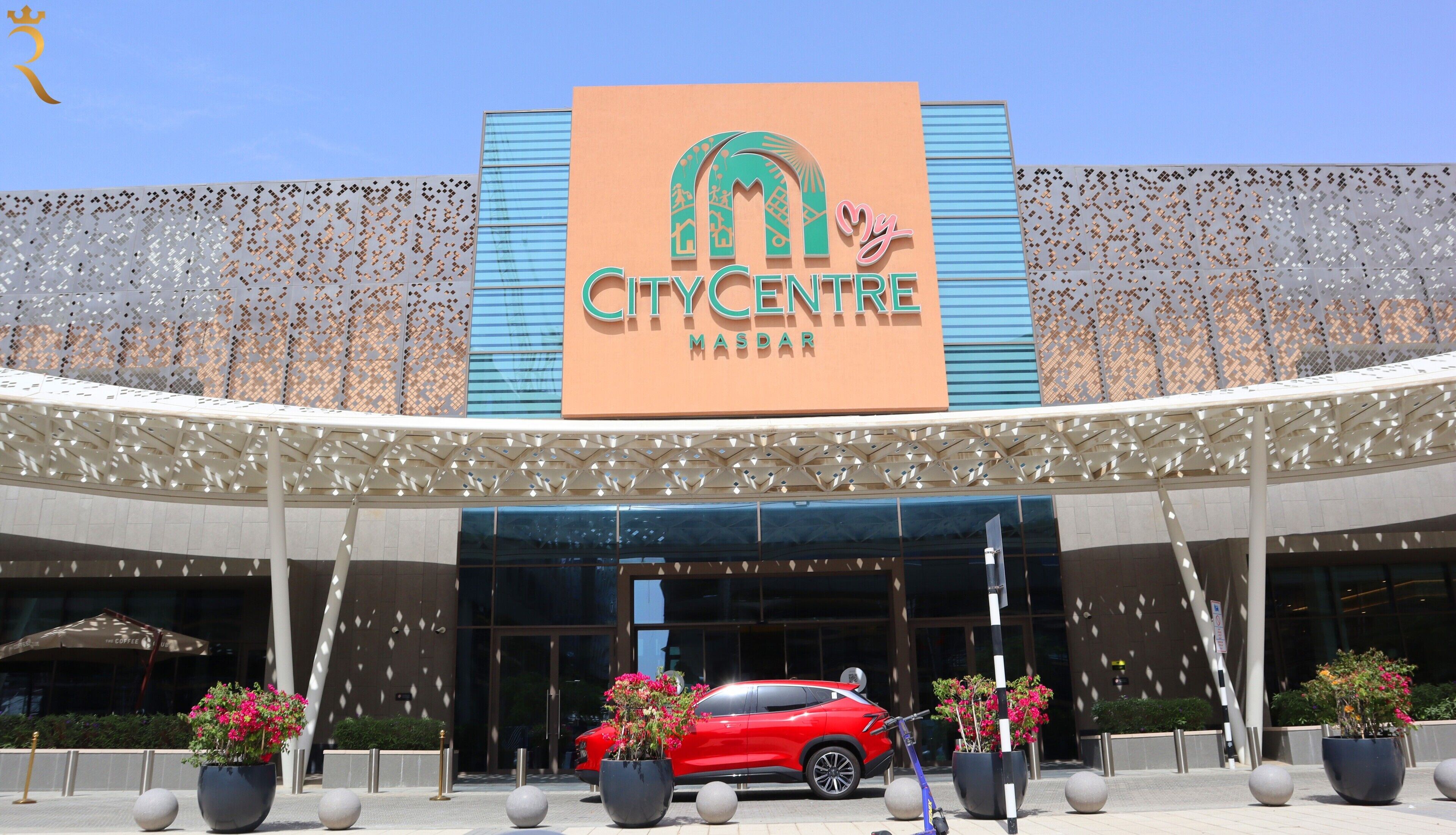 La façade extérieure du bâtiment City Centre Masdar, avec une voiture rouge garée devant.