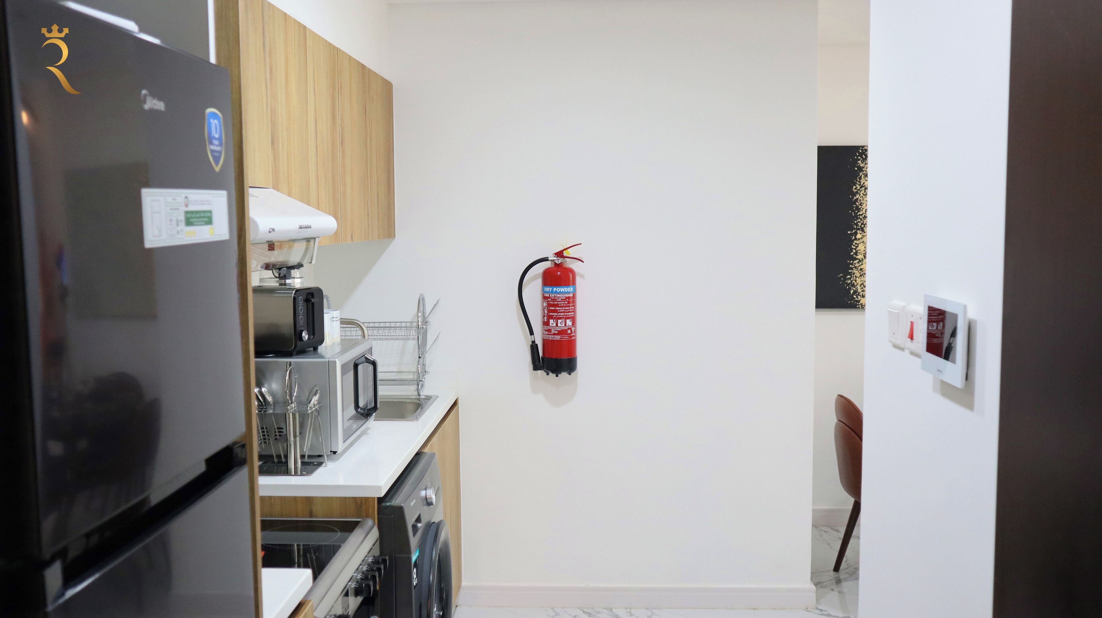 A compact kitchen with a refrigerator, microwave, toaster, and sink. A fire extinguisher is mounted on the wall.