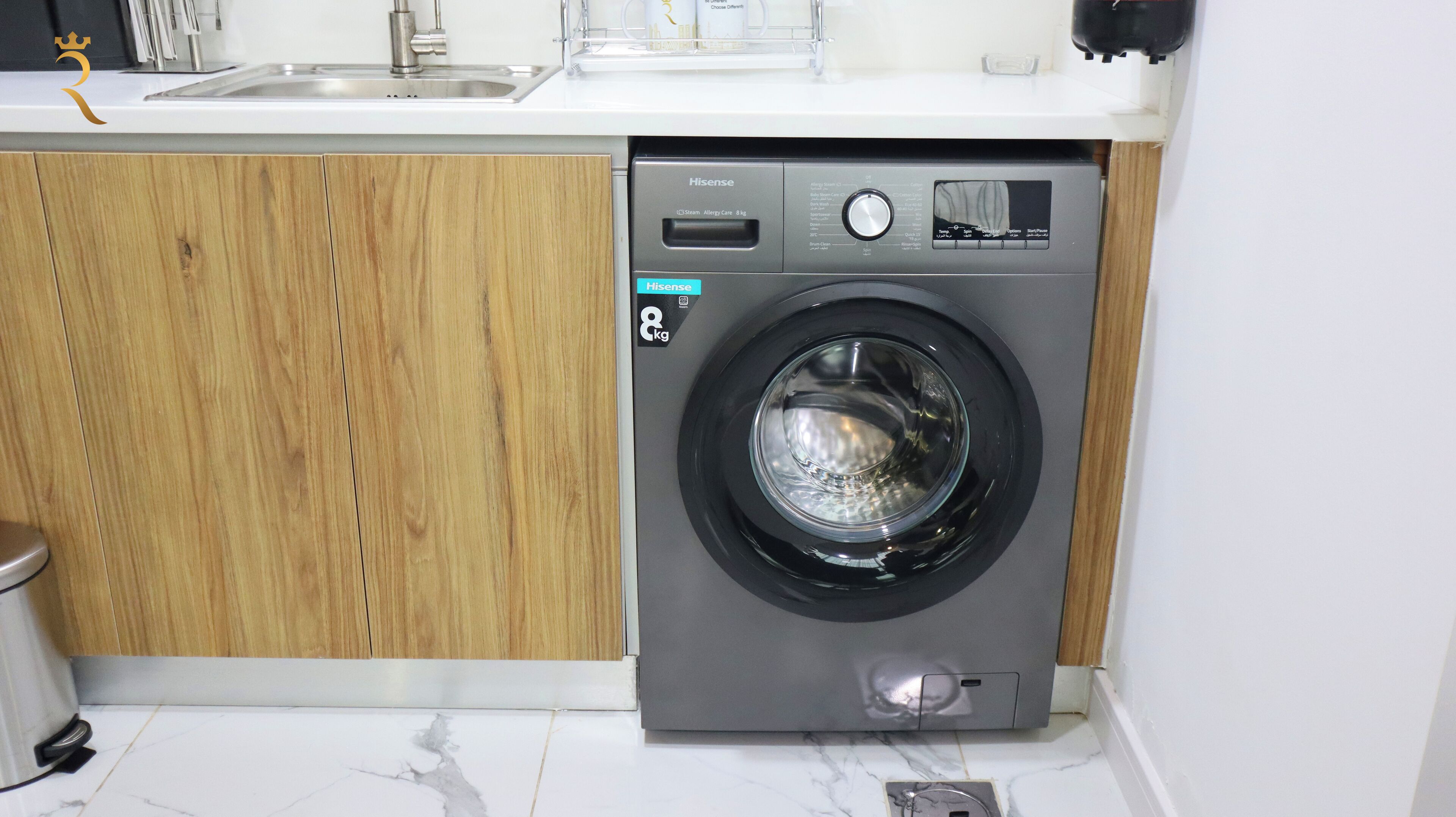 Un lave-linge Hisense compact doté d’un panneau de commande numérique, installé dans une cuisine avec des meubles en bois et un plan de travail blanc.