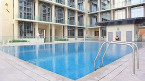 A modern indoor swimming pool with clear blue water, surrounded by a tiled deck and glass railings. - Masdar Oasis 2 Design Apartments By Rhh (Abu Dhabi)