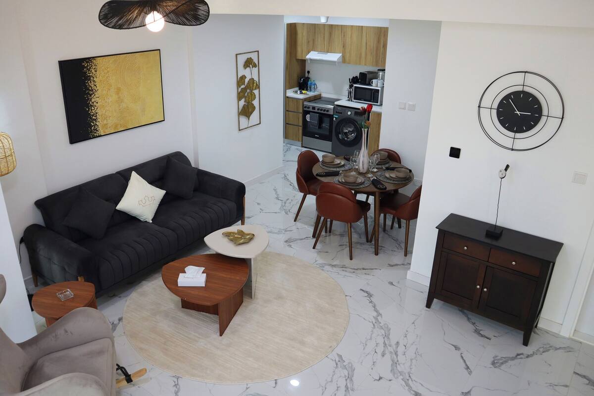 A modern living room with a black sofa, a round coffee table, and a dining area with a table set for four.
