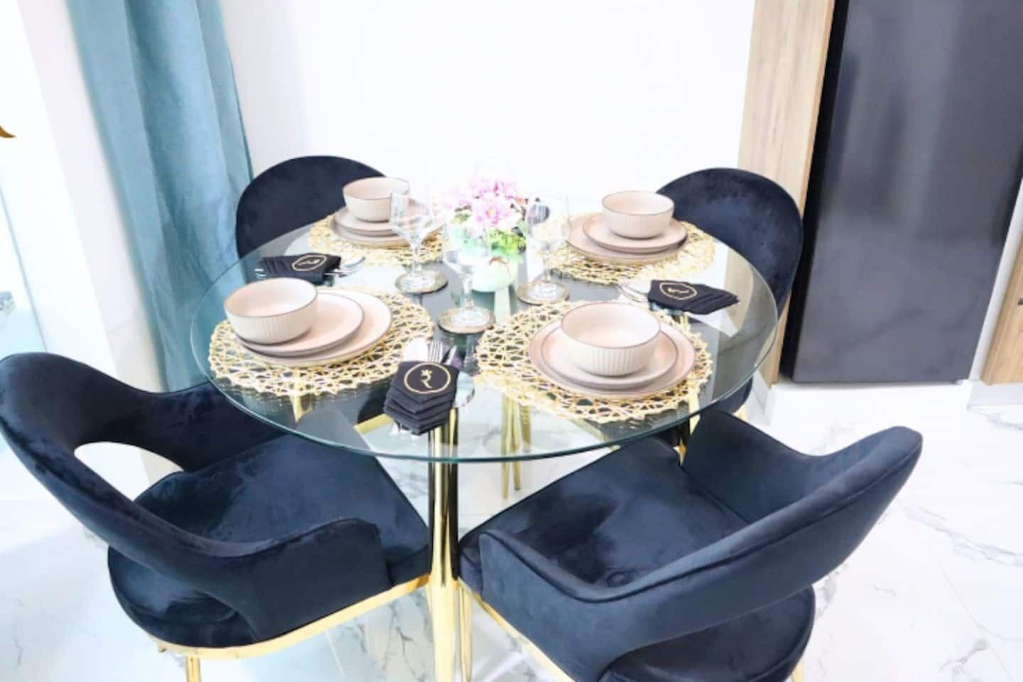 Una mesa redonda de cristal con base dorada, rodeada de sillas de terciopelo negro.