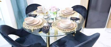 Una mesa redonda de cristal con base dorada, rodeada de sillas de terciopelo negro.
