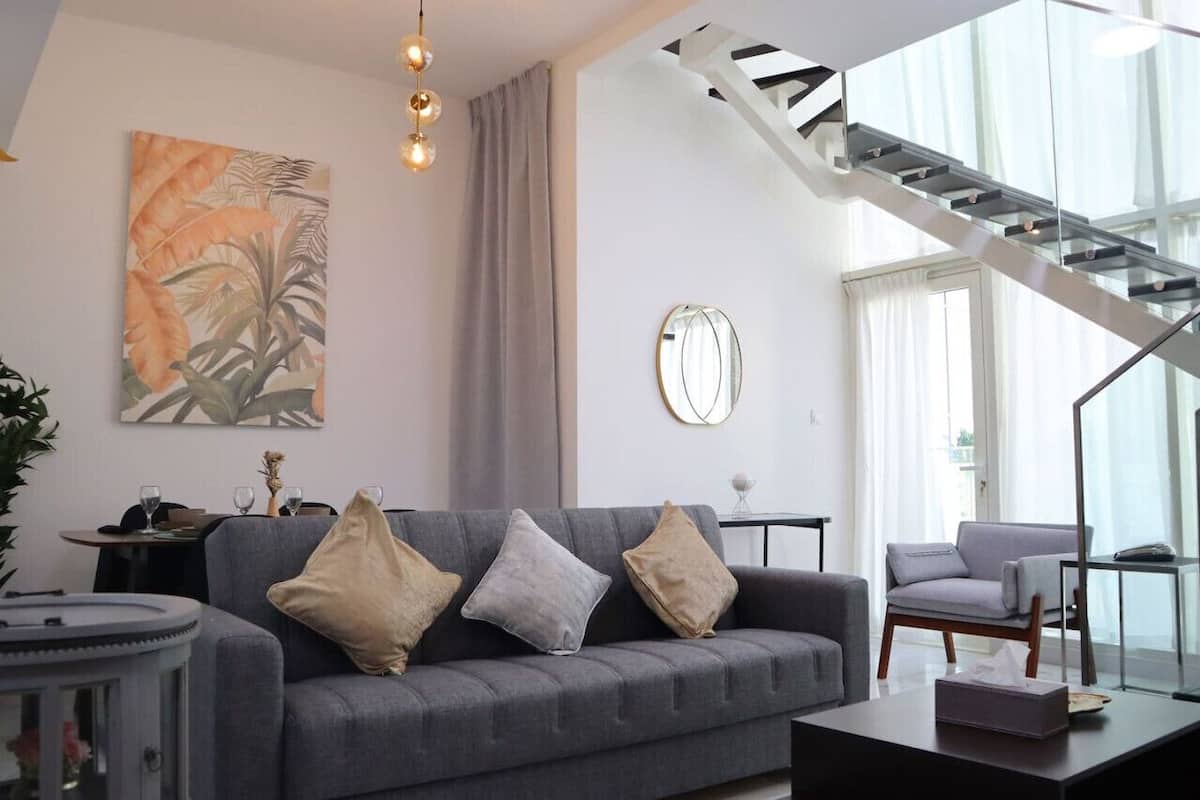 A modern living room with a grey sofa, a round mirror, and a staircase leading to an upper level.