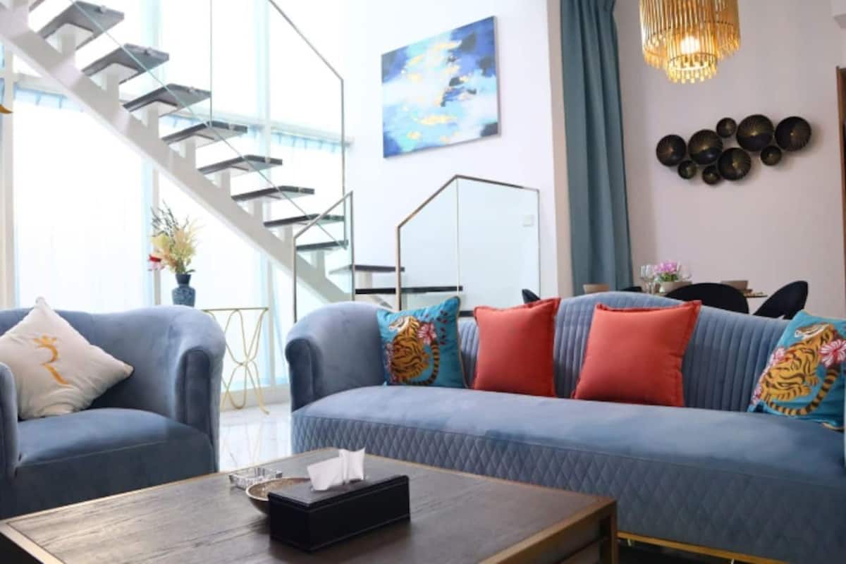 A modern living room with a blue sofa, two armchairs, a coffee table, and a staircase leading to an upper level.