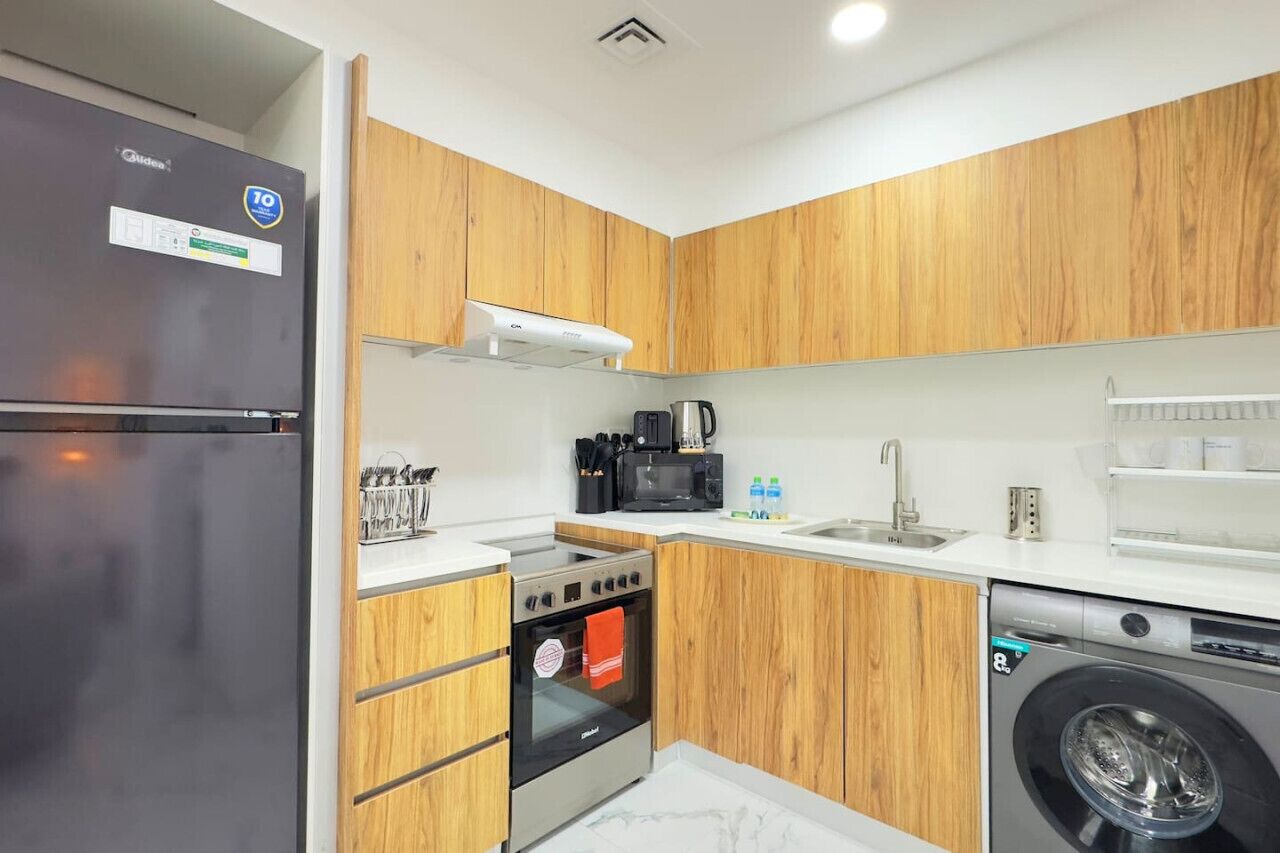 A compact kitchen with wooden cabinets, a stainless steel refrigerator, a built-in oven, a microwave, a sink, and a washing machine.