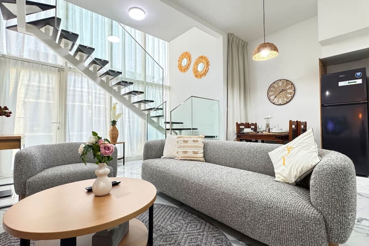 A modern living room with a grey sofa, a round coffee table, and a staircase leading to an upper floor.