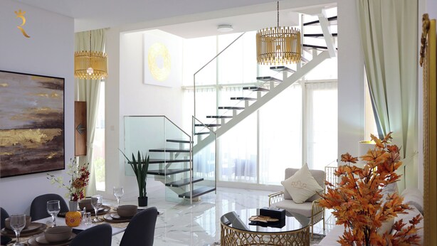 A modern living room with a glass staircase, a dining area with a table set for two, and a large abstract painting on the wall. - Masdar Oasis 2 Design Apartments By Rhh (Abu Dhabi)