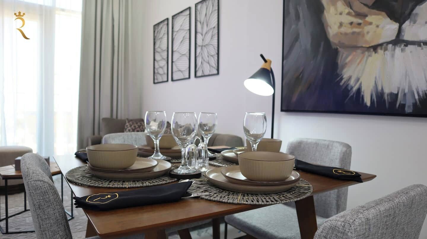 Une table à manger dressée avec des assiettes, des bols et des verres, agrémentée d’une lampe et d’une œuvre d’art accrochée au mur.