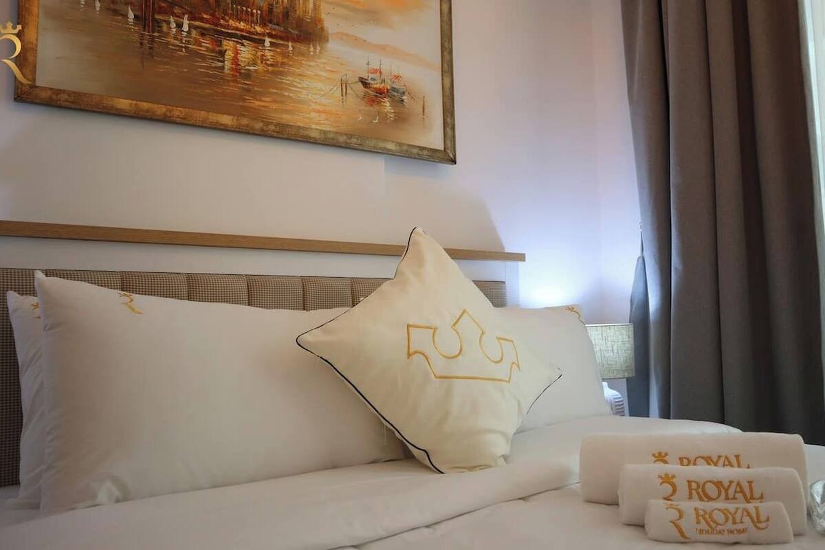 A hotel room with a bed, pillows, a painting, and a window with curtains.