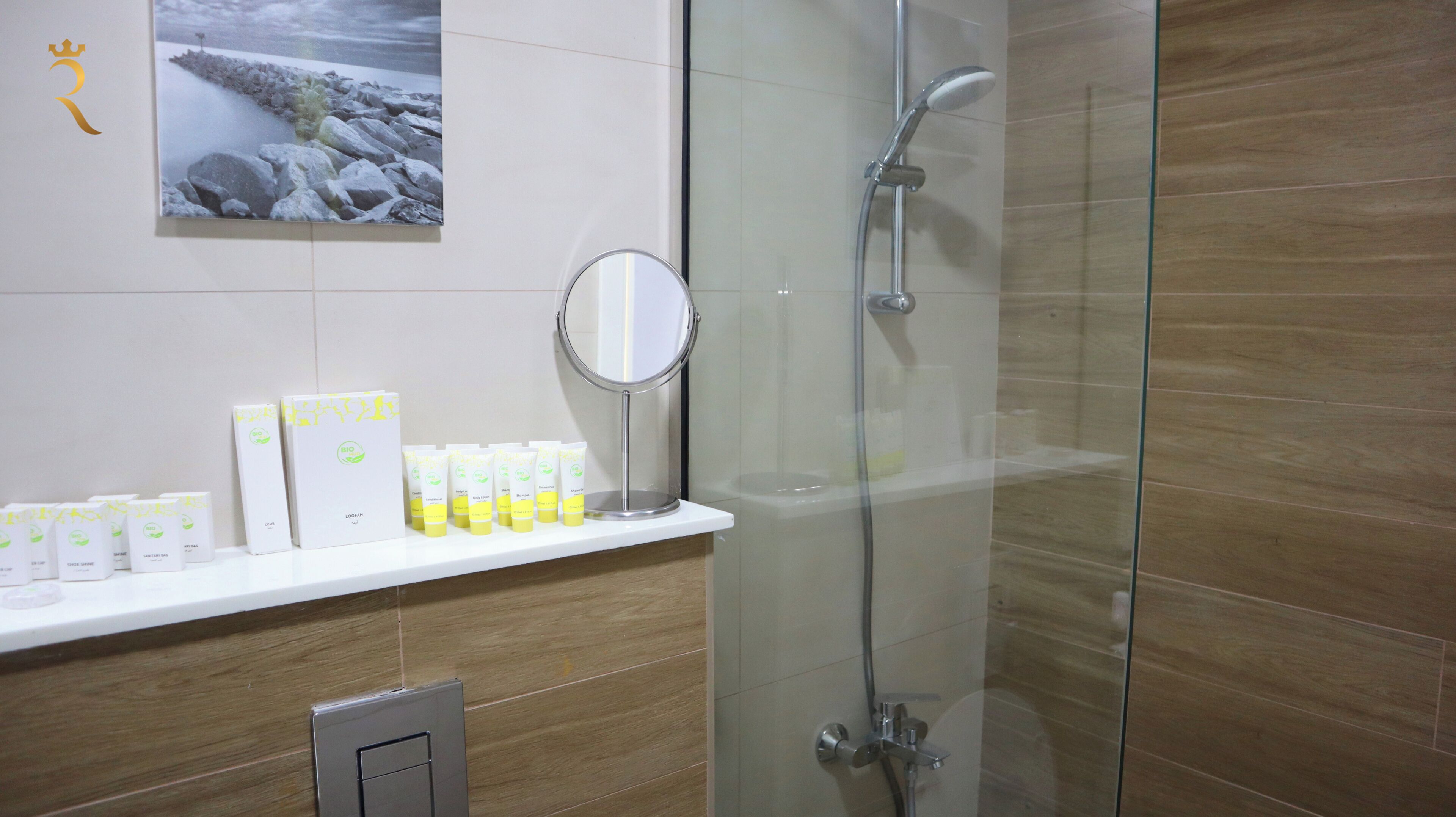 Une salle de bain avec une douche à parois de verre, une étagère blanche où sont rangés les articles de toilette et un tableau encadré au mur.