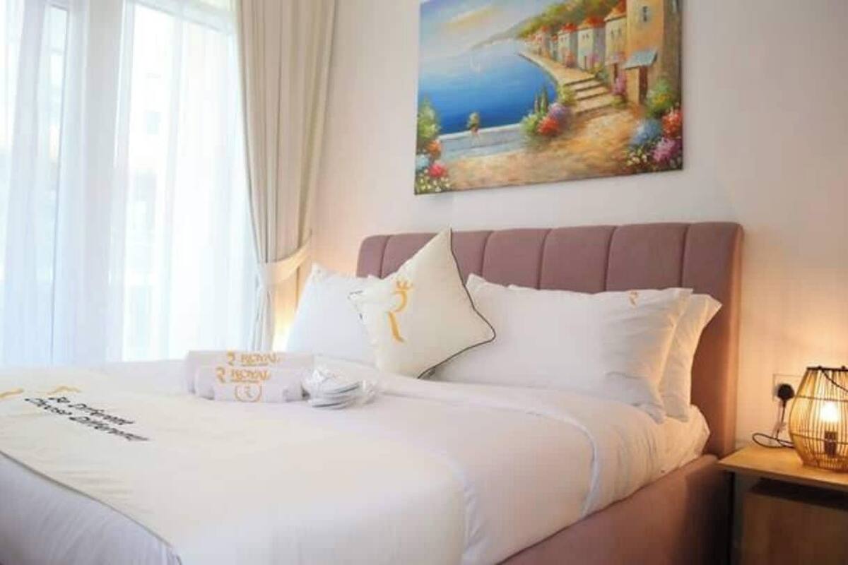 A neatly made bed with a white comforter and pillows, a bedside table with a lamp, and a painting of a coastal scene on the wall.