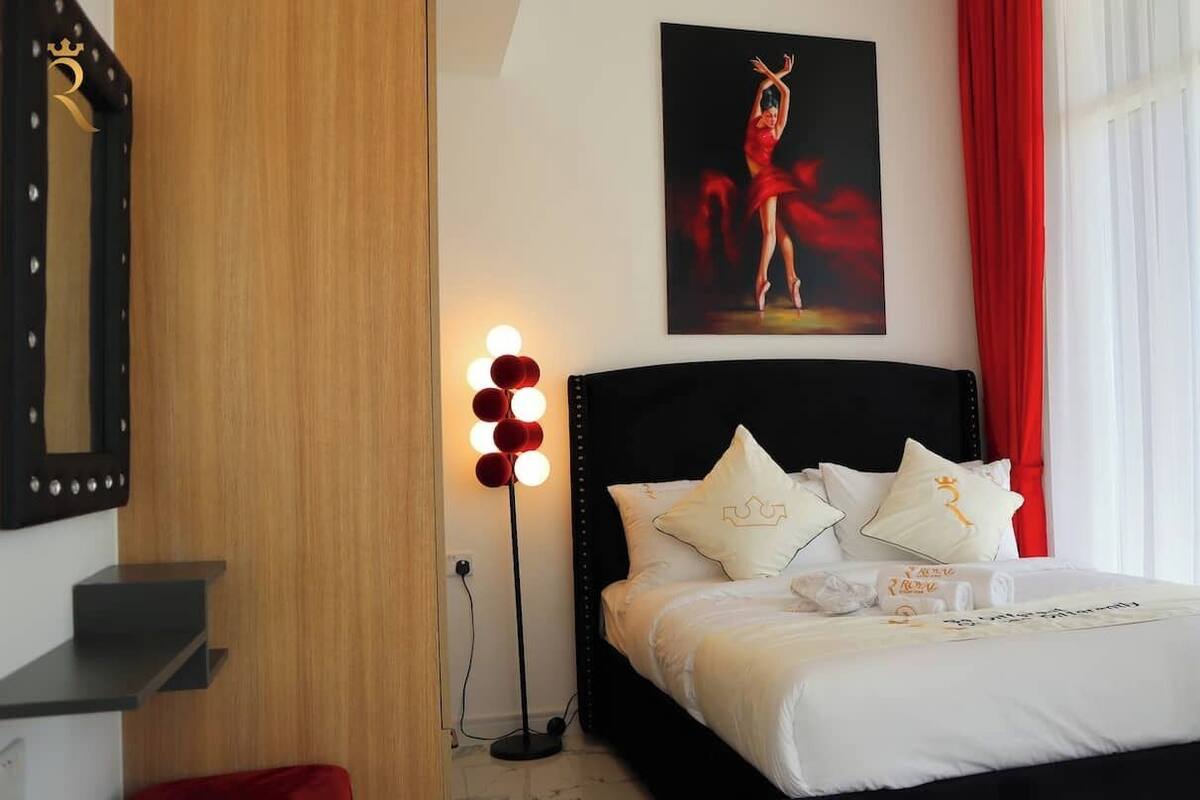 A hotel room with a bed, a nightstand, a mirror, a painting, and a red curtain.