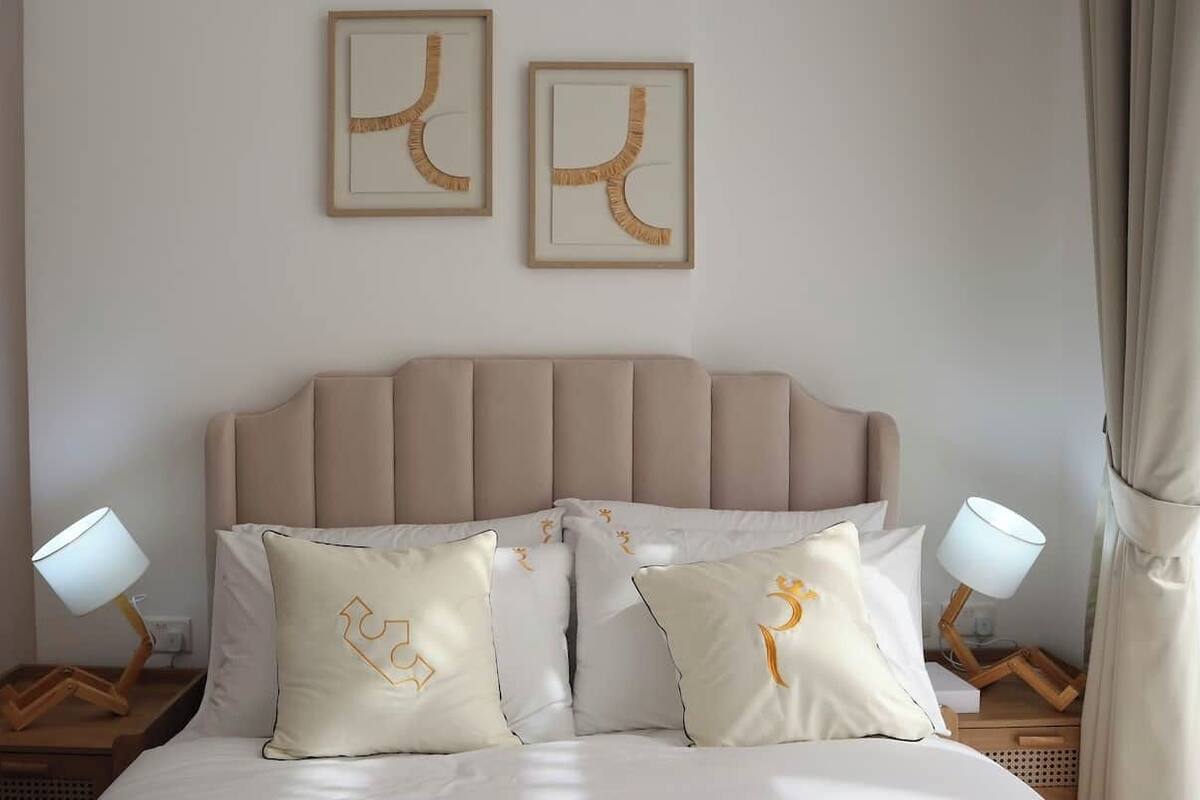 A neatly made bed with a headboard, two bedside lamps, and decorative pillows with a unique design.