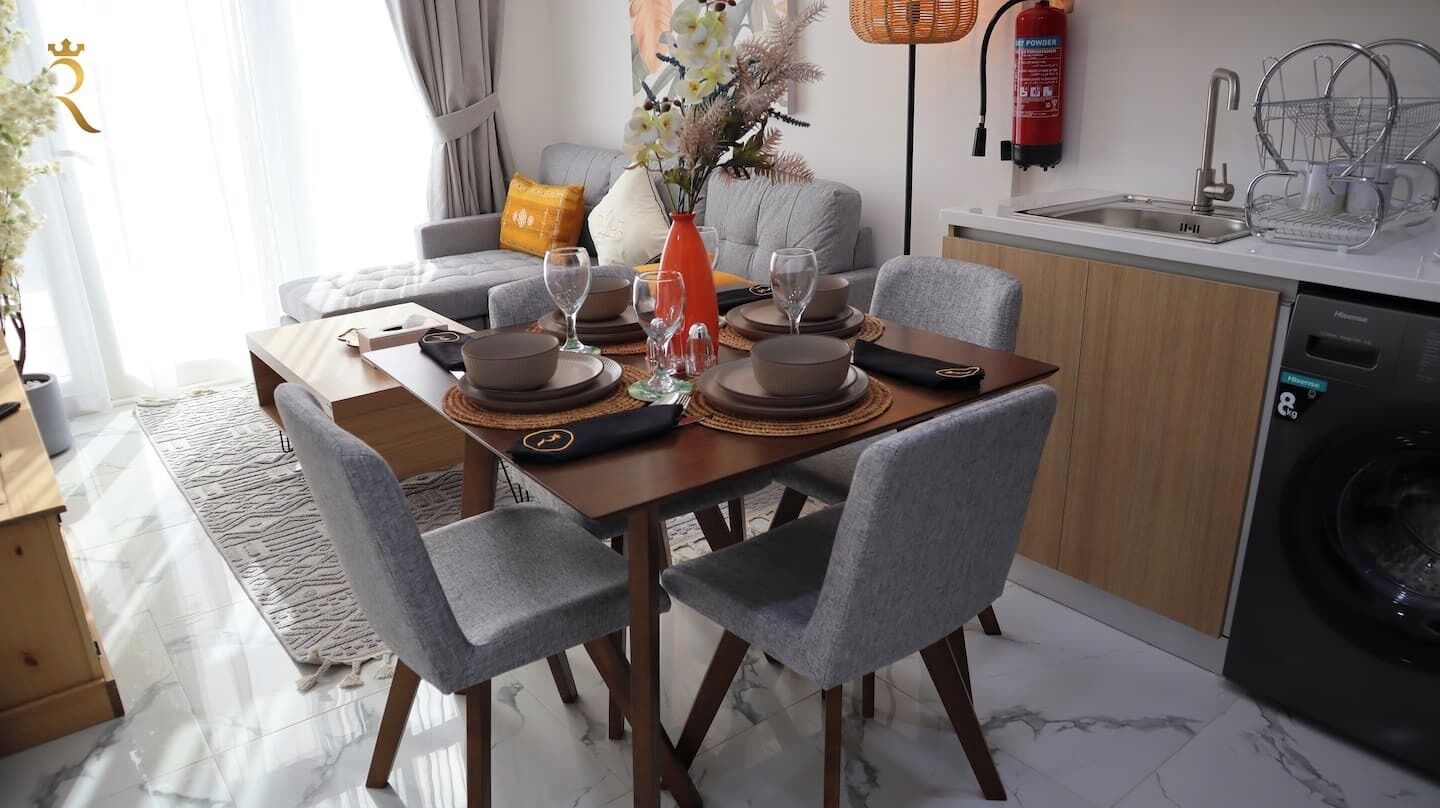Un coin repas avec une table dressée pour quatre personnes, des chaises grises, un vase avec des fleurs et un extincteur fixé au mur.