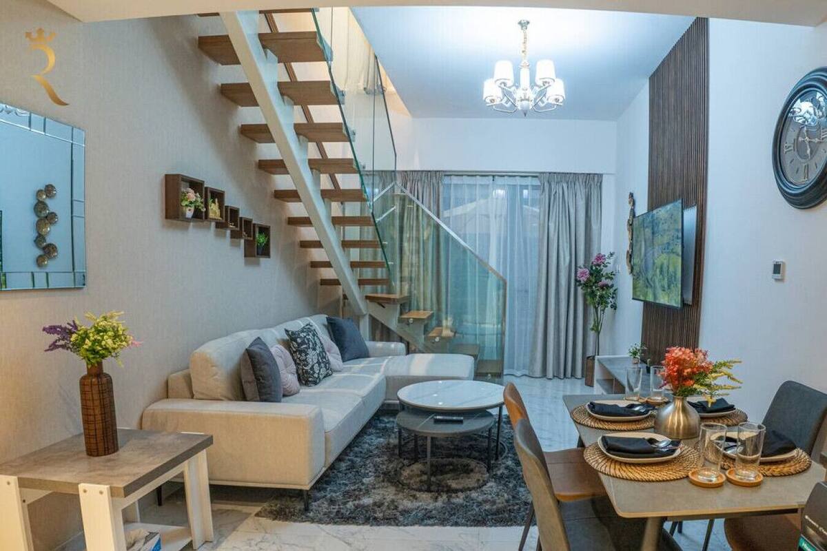 A modern living room with a sofa, coffee table, and dining area. A staircase leads to an upper level.