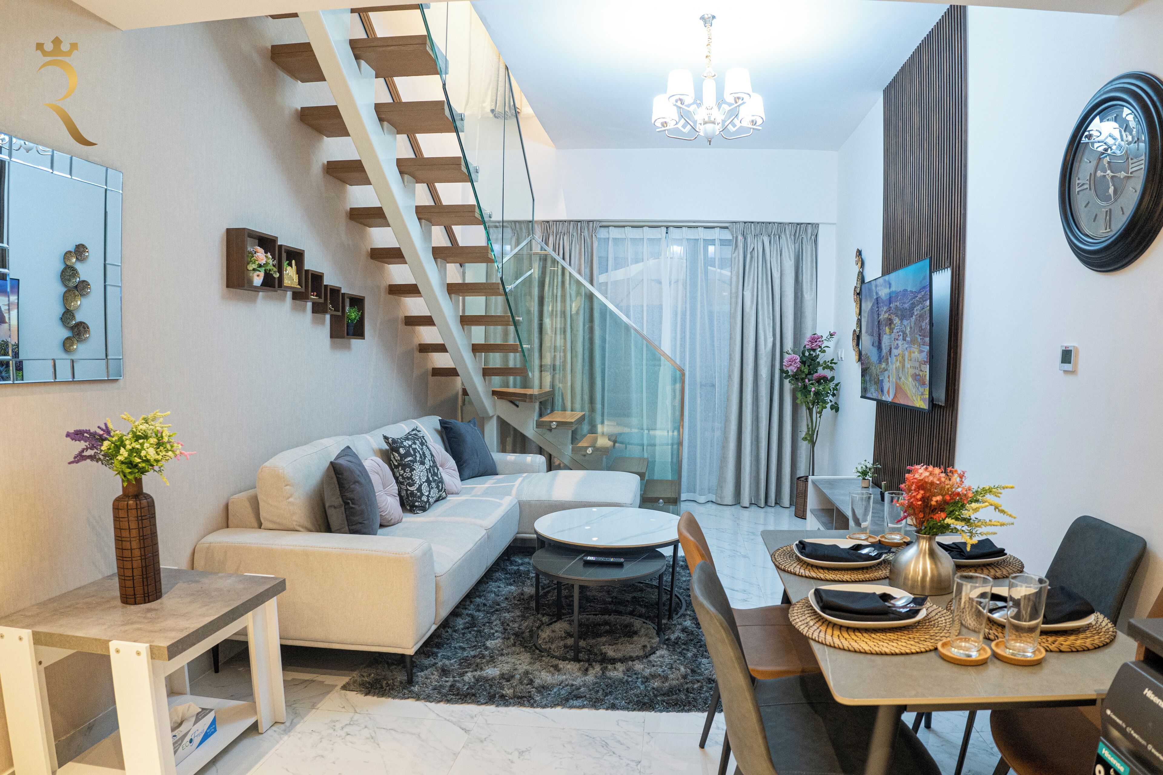 Ein modernes Wohnzimmer mit Treppe, einem Essbereich mit Tisch für zwei Personen und einer großen Uhr an der Wand.